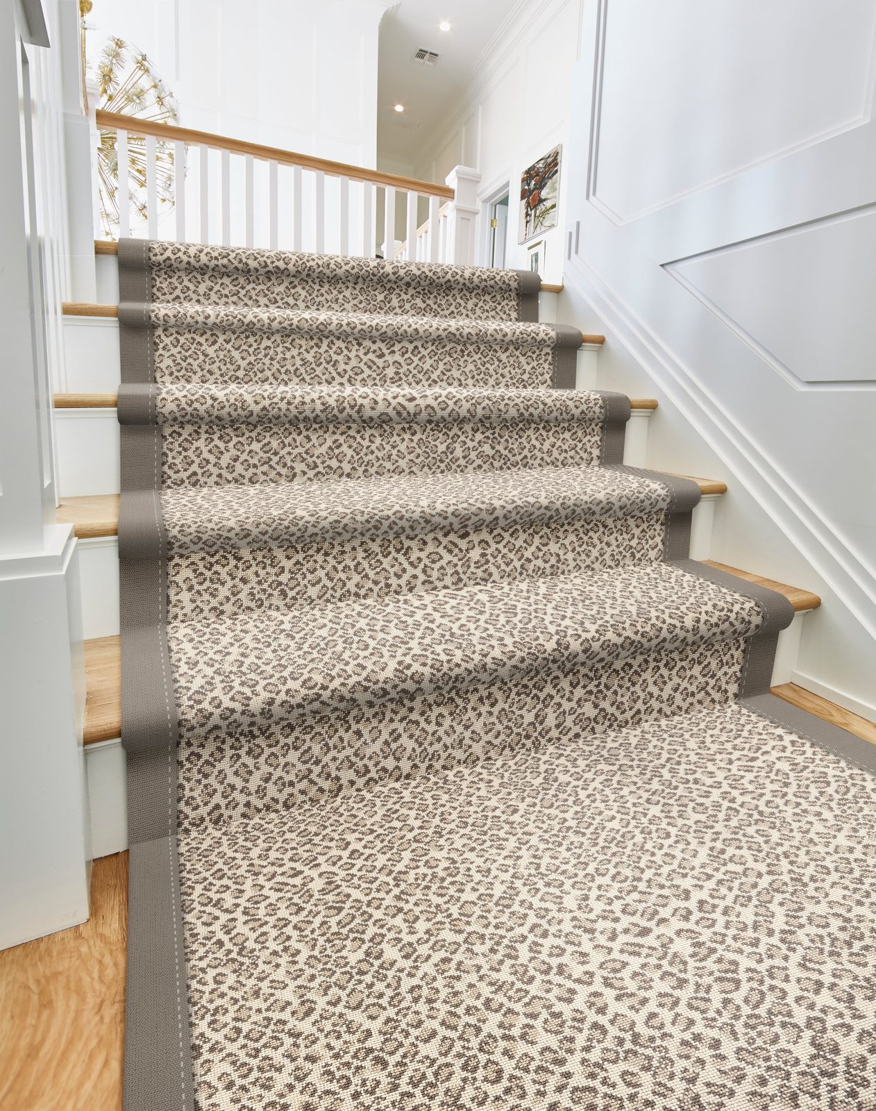 Snow-leopard-pattern stair runner with gray bound edges running up white-painted stairs with light wood treads showing on each side